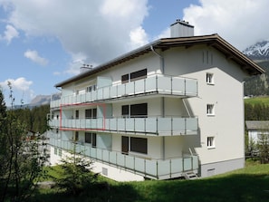 Un immeuble à plusieurs étages doté de balcons, d’un escalier et ayant une chaîne de montagnes en arrière-plan.