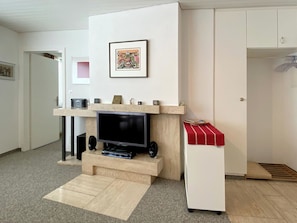 Un salon équipé d’un téléviseur à écran plat, d’une cheminée, d’une petite table recouverte d’une nappe rouge et d’un meuble blanc.