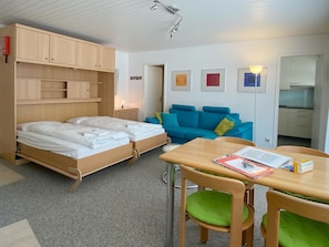 Une chambre avec deux lits, un canapé bleu, une table avec des chaises et un coin cuisine.