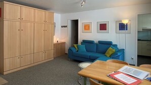 Un espacio habitable compacto con un armario de madera, un sofá azul, una mesa de comedor con un libro y una lámpara en el techo.