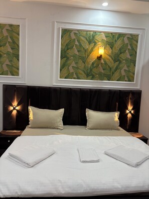 Une chambre d’hôtel avec un grand lit, deux lampes de chevet et deux décorations murales encadrées représentant des motifs de feuilles.