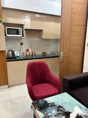 Une cuisine moderne équipée d’un four à micro-ondes, d’une bouilloire et d’une machine à café. On y trouve une chaise rouge et une table en verre au motif marbré.
