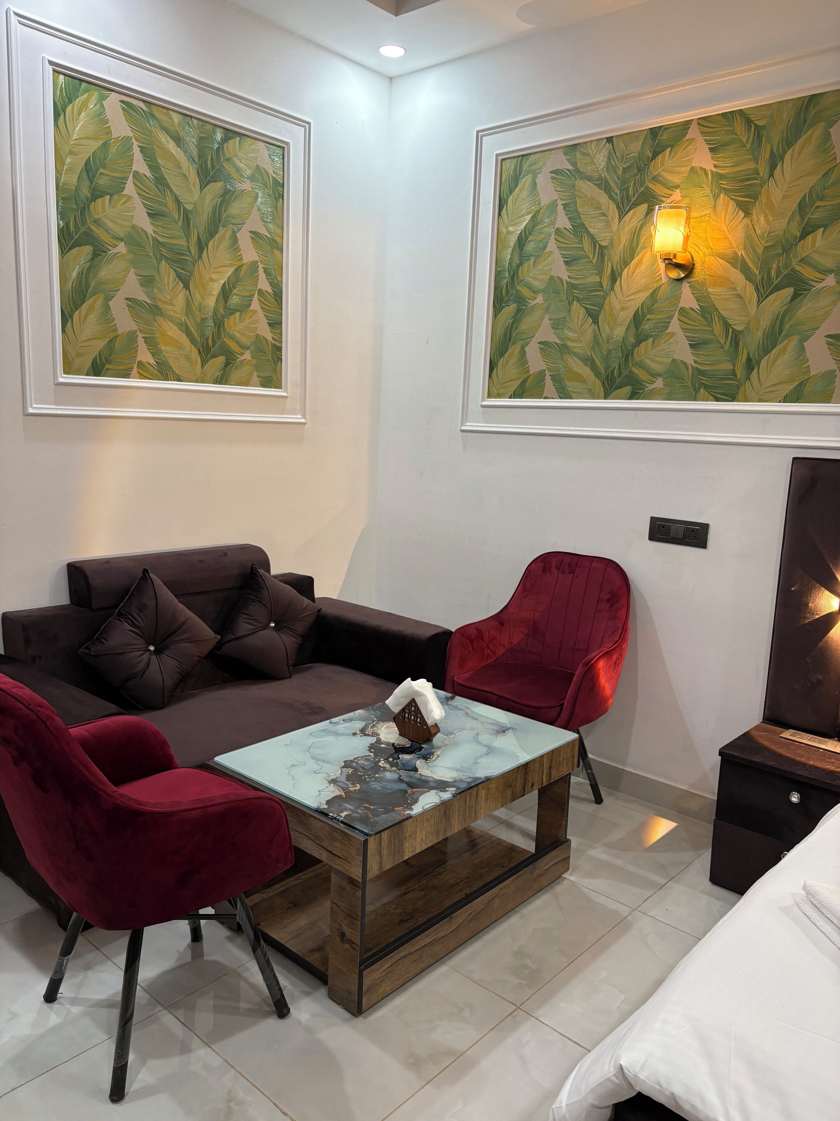 A modern room with a sofa, two red chairs, a coffee table, and two large leaf-patterned paintings on the walls.