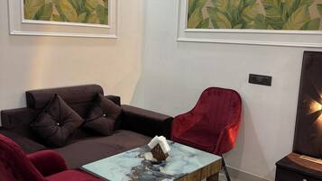 A modern room with a sofa, two red chairs, a coffee table, and two large leaf-patterned paintings on the walls.