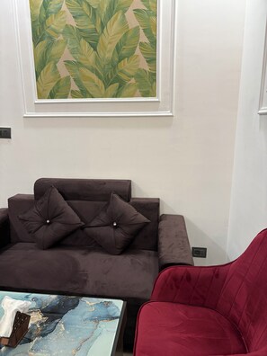 Un salon avec un canapé marron, un fauteuil rouge, une table basse en marbre et une décoration murale à motifs de feuilles.