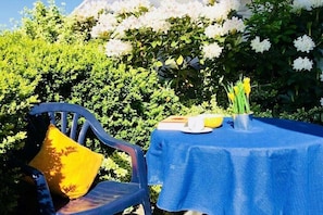 Ein Tisch mit blauer Tischdecke, ein Stuhl mit gelbem Kissen und eine Vase mit gelben Blumen.