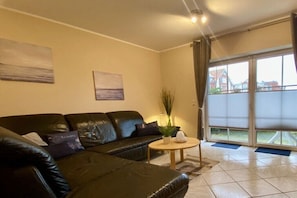 Ein Wohnzimmer mit einer schwarzen Ledersofa, einem kleinen runden Tisch und einer großen Schiebeglastür, die auf einen Balkon führt.