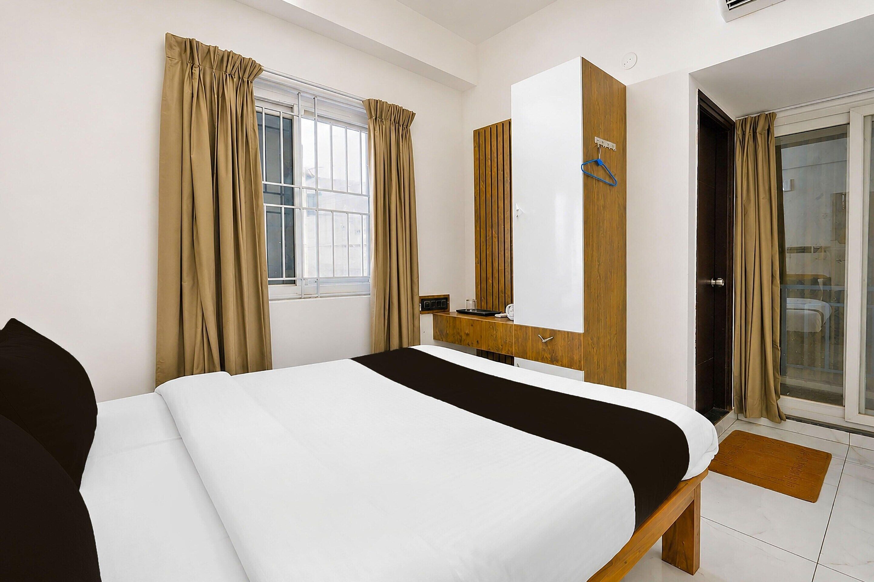 A hotel room with a bed, a wooden dresser, a mirror, a window with curtains, and a door leading to a balcony.