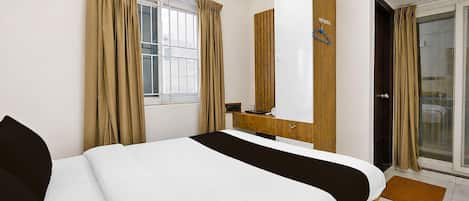 Habitación de hotel con una cama, cómoda de madera, espejo, ventana con cortinas y puerta que da a un balcón.