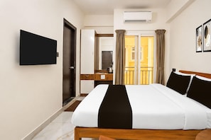 A hotel room with a bed, a desk, a television, and an air conditioning unit. - Classic Add In Rooms (Bengaluru)