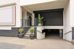 A modern building entrance with a staircase, potted plants, and a glass railing.