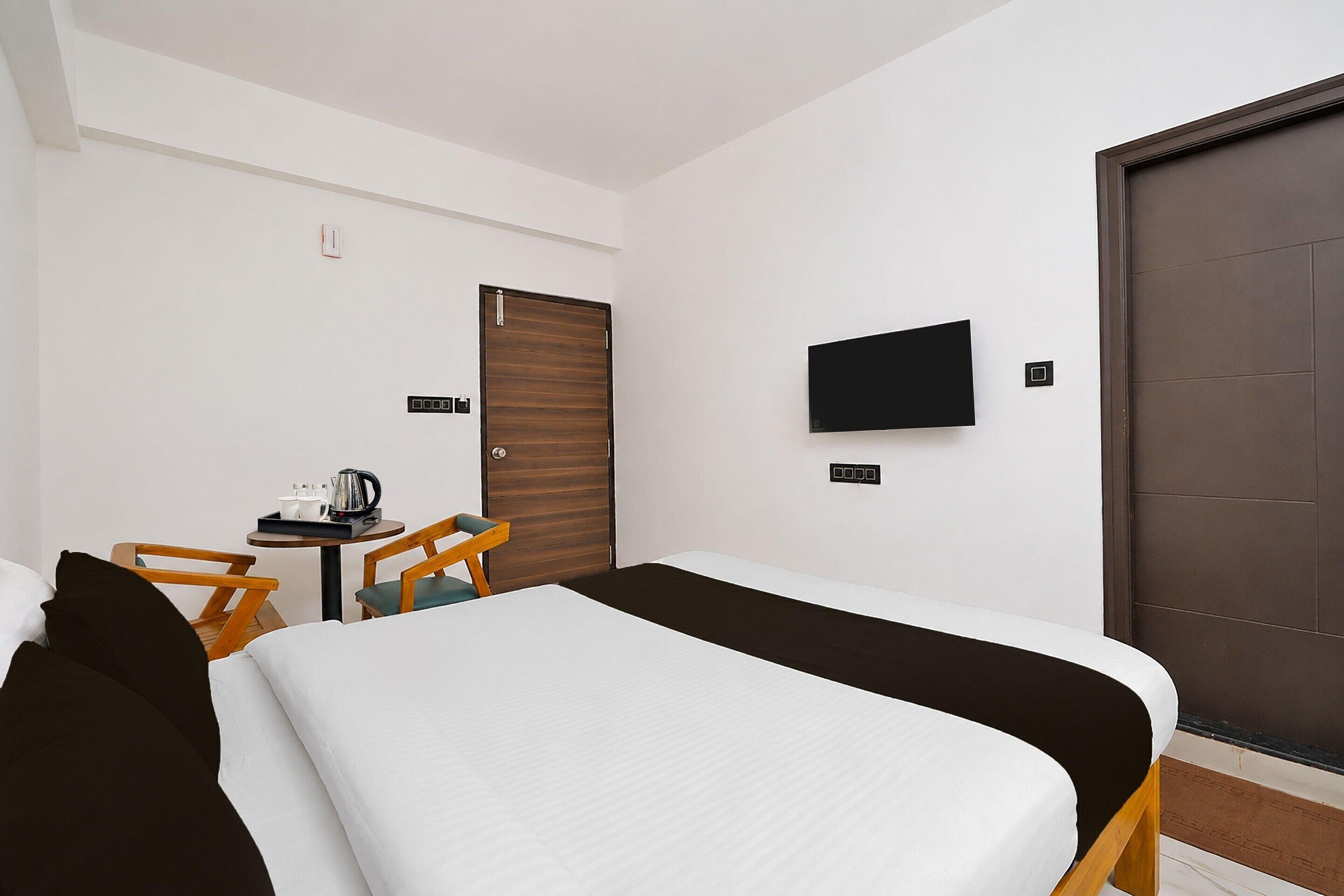 A hotel room with a bed, a desk with a chair, a television mounted on the wall, and a door.