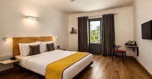 A hotel room with a bed, a desk, a chair, a TV, and a window with curtains. - Classic Add In Rooms (Bengaluru)