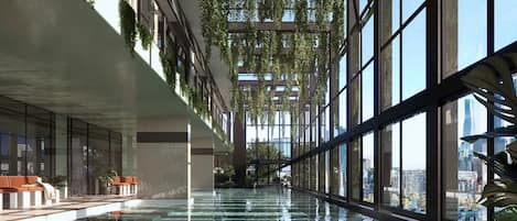 Piscina interior con paredes de vidrio, techo alto y plantas colgantes.