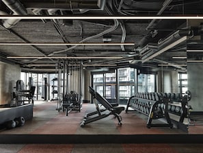 Ein Fitnessstudio mit Trainingsgeräten, großen Fenstern und einer modernen Industriedecke.