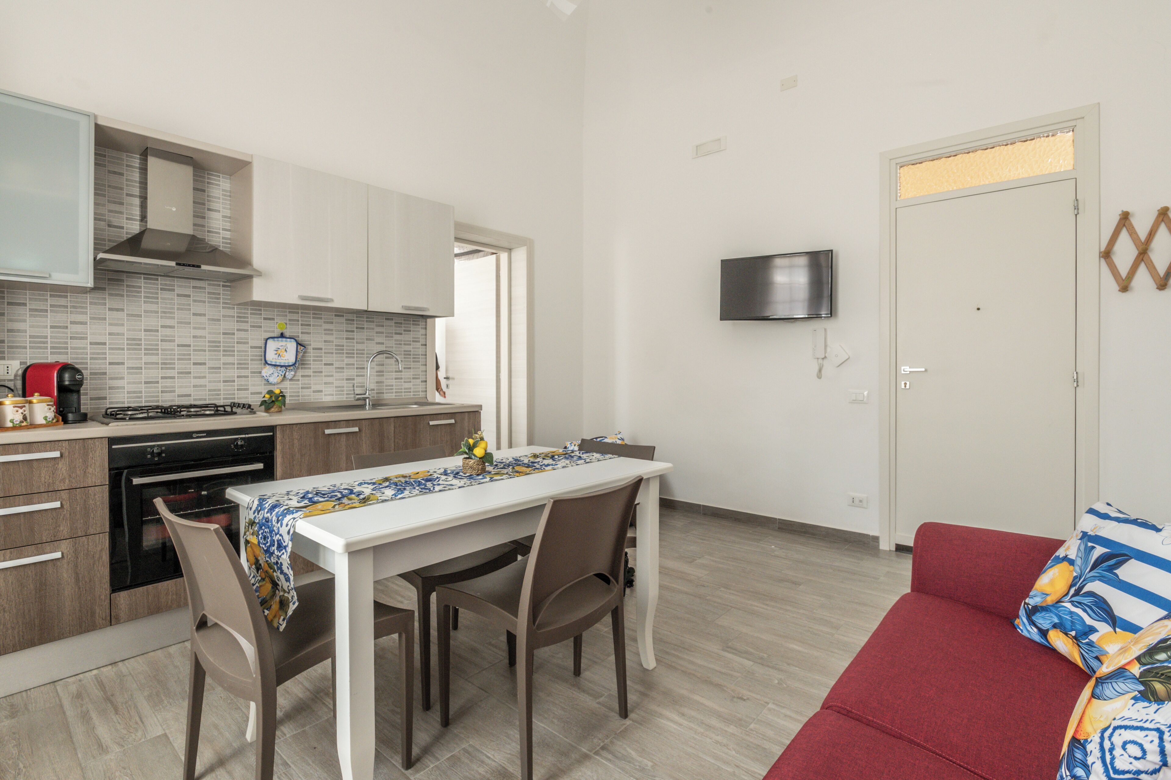 A modern kitchen with a dining table, chairs, and a red sofa.