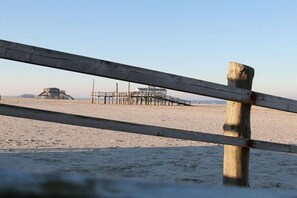 Ein Strand mit einer Holzbank, einem Steg und einem Gebäude im Hintergrund.