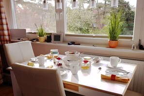 Ein Essbereich mit einem für das Frühstück gedeckten Tisch, einem Laptop, einer Pflanze und einem Fenster mit Blick auf Bäume.