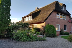 Ein Haus mit einem Strohdach, Backsteinmauern und einem Schotterweg.