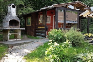 A rustic cabin with a stone oven, wooden exterior, and a garden with flowers.