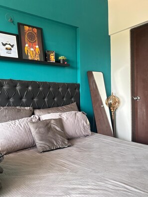 A bedroom with a tufted headboard, a bed with grey bedding, a teal wall, and a door with a golden handle. - Chillout space-Palghar with private JACUZZI! (Velgaon)