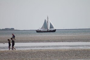 Ein Strand mit einem Segelboot, Personen, die spazieren gehen, und Windkraftanlagen in der Ferne.