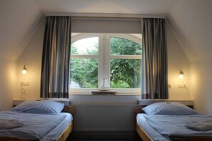 Ein Zimmer mit zwei Betten, einem fensterbelaubten Fenster und einem Heizkörper darunter.