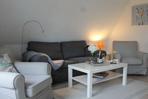 Ein Wohnzimmer mit einem grauen Sofa, einem weißen Couchtisch und einem karierten Sessel.
