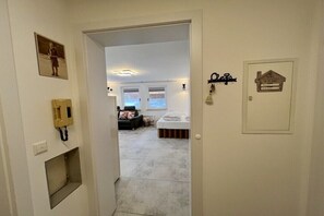 Ein Flur, der in ein Schlafzimmer mit Bett, Nachttisch und festmontiertem Telefon führt.