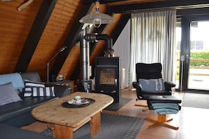 Ein gemütlicher Raum mit einer Couch, einem Sessel, einem Tisch, einem Kamin und einem Fenster mit Vorhängen.