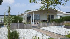Et moderne hus med en overdækket terrasse, grusvej og et træ i forhaven.