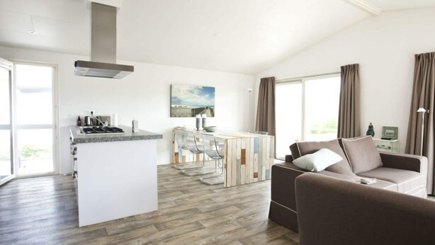 Et moderne køkken med en central ø, et spiseområde med barstole, en sofa og et stort vindue med gardiner.