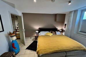 Ein Schlafzimmer mit einem Bett, einem Nachttisch, einer Lampe, einem Fenster und einer dekorativen Statue.