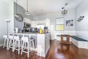 A modern kitchen with white cabinetry, a central island with bar stools, a built-in bench, and a dining table. - Jax Beach Zen Retreat – Walk to Ocean & Pier (Jacksonville Beach)