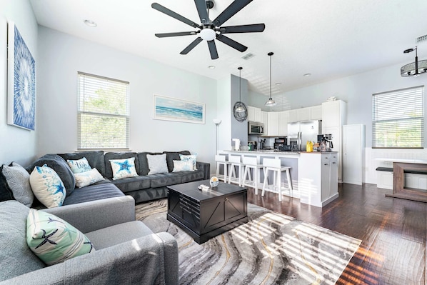 A modern living room with a sofa, coffee table, and a kitchen area in the background. - Jax Beach Zen Retreat – Walk to Ocean & Pier (Jacksonville Beach)