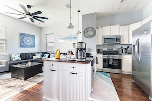 A modern kitchen with white cabinets, stainless steel appliances, and a central island with a coffee maker. - Jax Beach Zen Retreat – Walk to Ocean & Pier (Jacksonville Beach)