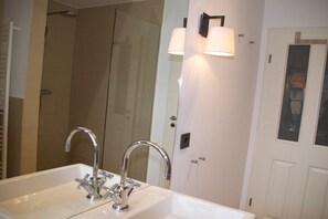 Ein Badezimmer mit einem Doppelwaschbecken, einer Dusche und einem Spiegel mit Wandleuchten.