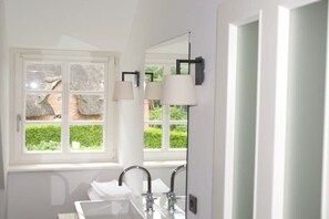 Een badkamer met een raam, twee wasbakken en twee wandlampen.