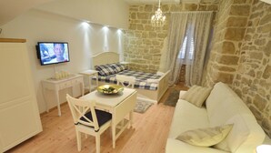 A cozy room with a bed, a dining table with chairs, a television, and a stone wall. - Studios Villa Rossella 4 (Rovinj)