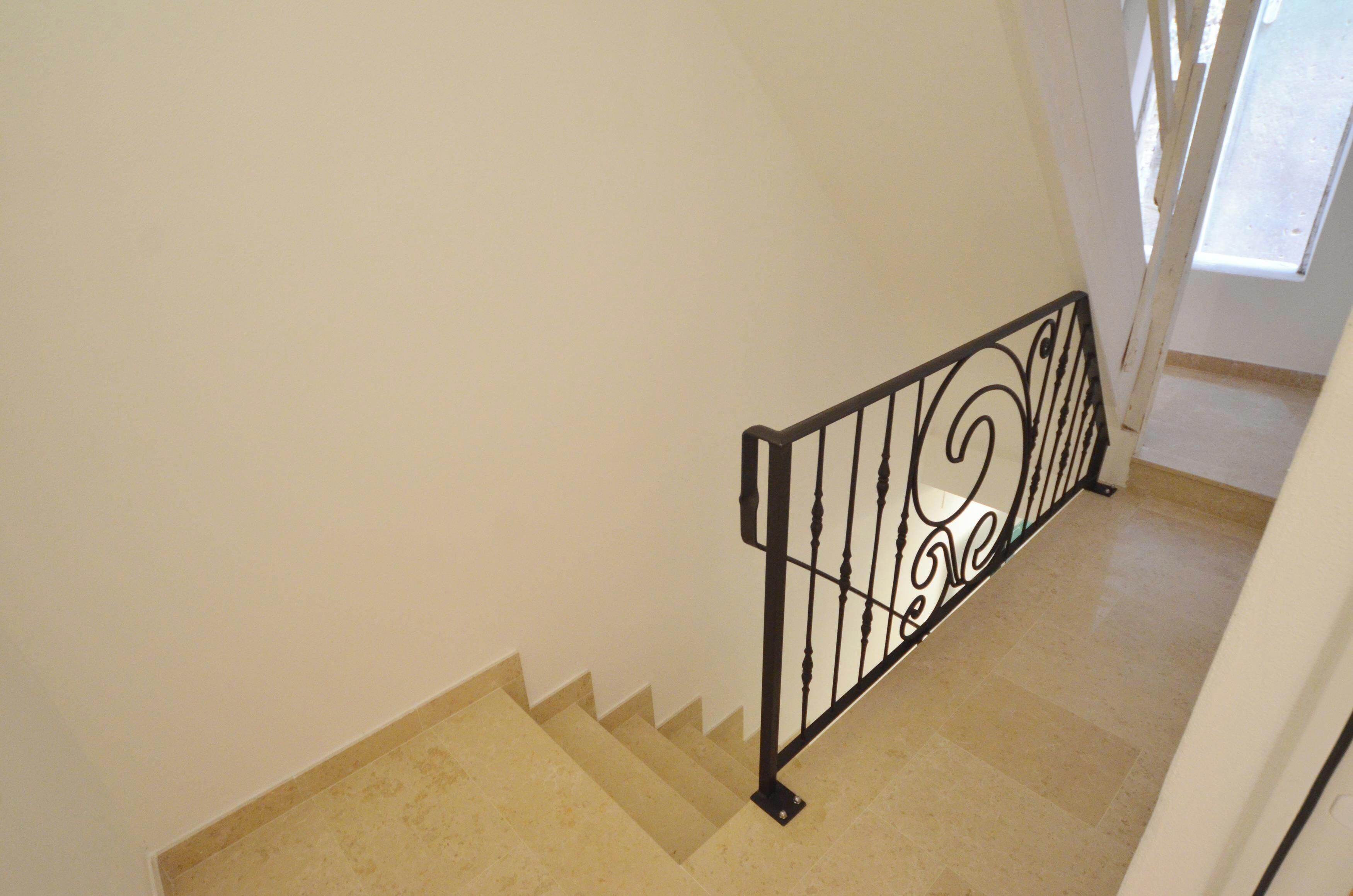 A staircase with a metal railing, beige steps, and white walls.