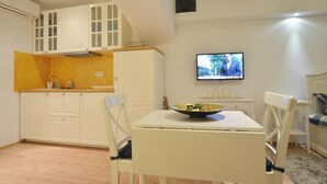 A compact kitchen with white cabinets, a dining table with chairs, and a television mounted on the wall. - Studios Villa Rossella 4 (Rovinj)