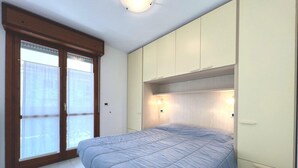 A bedroom with a bed, sliding doors, and built-in cabinets. - Well Equipped Holiday Home in Grado (Grado)