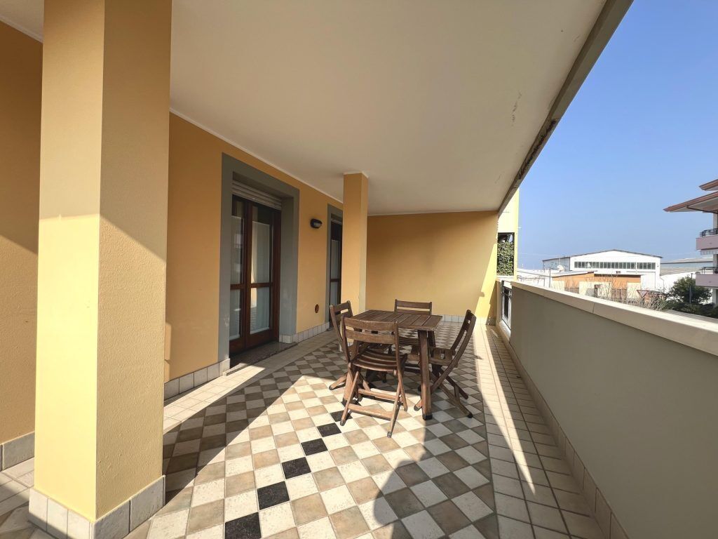 Uma varanda com chão xadrez, mesa e cadeiras de madeira, e uma porta.