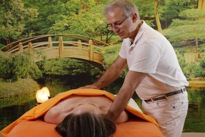 A person receiving a back massage in a room with a view of a bridge over water. - Herbert Ziegler Winery "Eulbusch" 2 (Maikammer)
