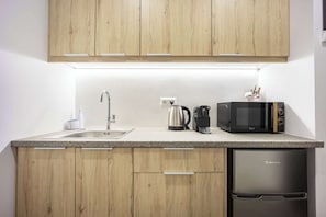 A compact kitchen with wooden cabinets, a stainless steel sink, a coffee maker, a kettle, a microwave, and a refrigerator. - Generous Studio Syntagma l Worn Entrance (Athina)
