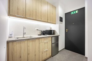Eine moderne Küche mit Holzschränken, einer Edelstahlspüle, einer Kaffeemaschine, einem Wasserkocher, einer Mikrowelle und einem schwarzen Kühlschrank.