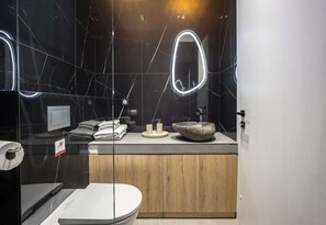 A modern bathroom with a marble backsplash, a wooden vanity, a large oval mirror, and a stone sink. - Generous Studio Syntagma l Worn Entrance (Athina)