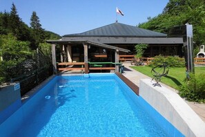 Ein Schwimmbad mit überdachtem Pavillon, umgeben von Grünpflanzen und einer Flagge.
