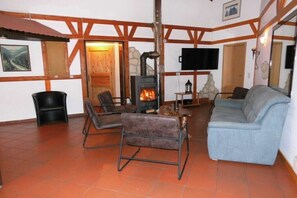 Ein gemütliches Wohnzimmer mit Kamin, Holzbalken, einer Couch und einem Fernseher.