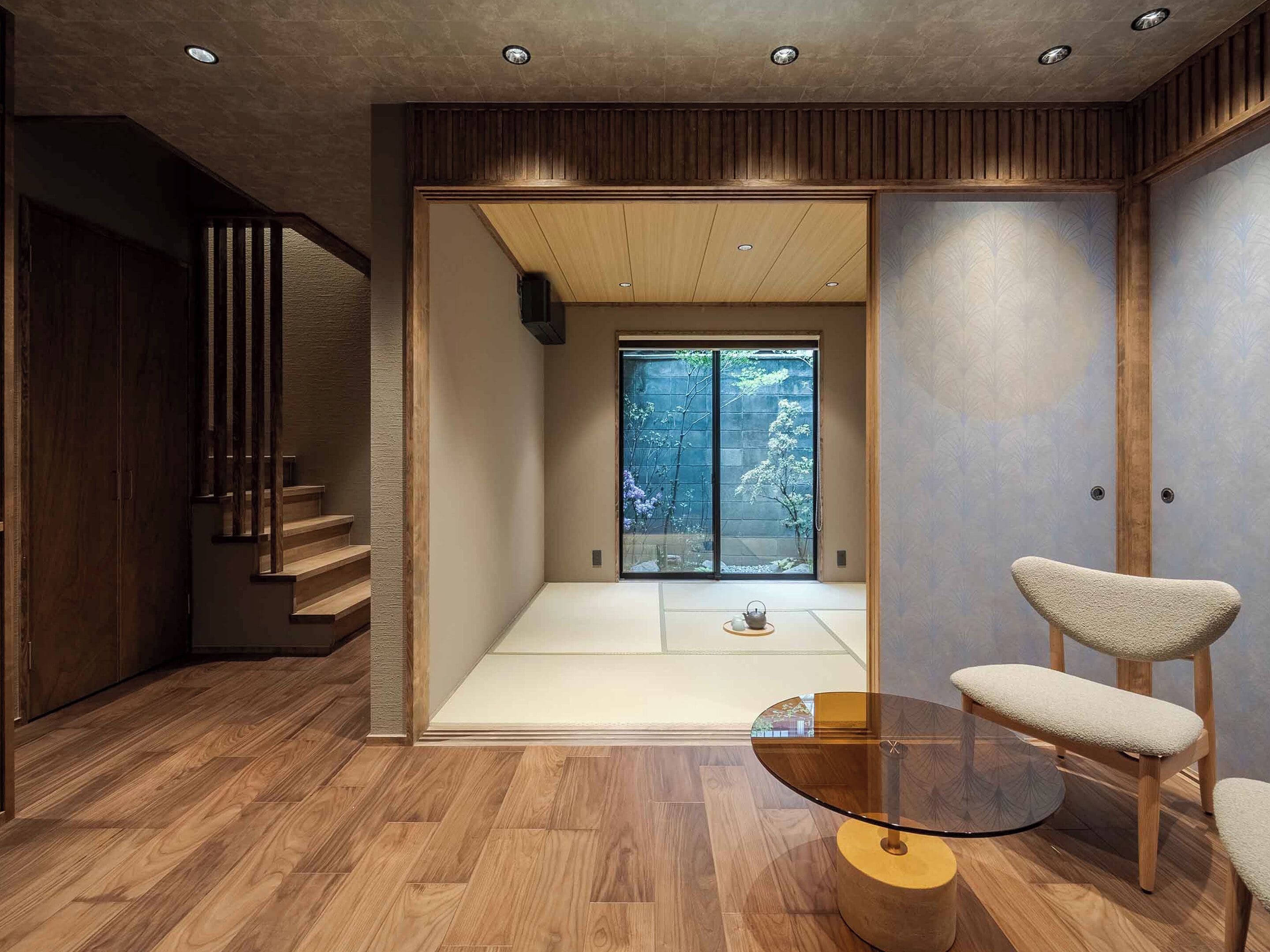 A modern interior with a wooden floor, a glass table, and a sliding door leading to a garden.